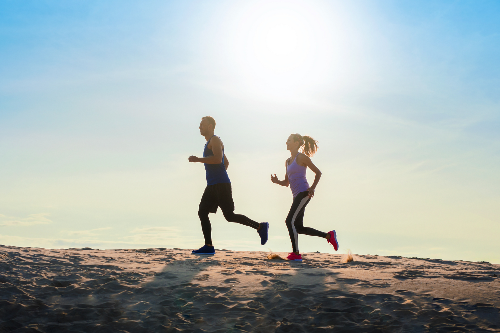 Two people running on a beach at sunset